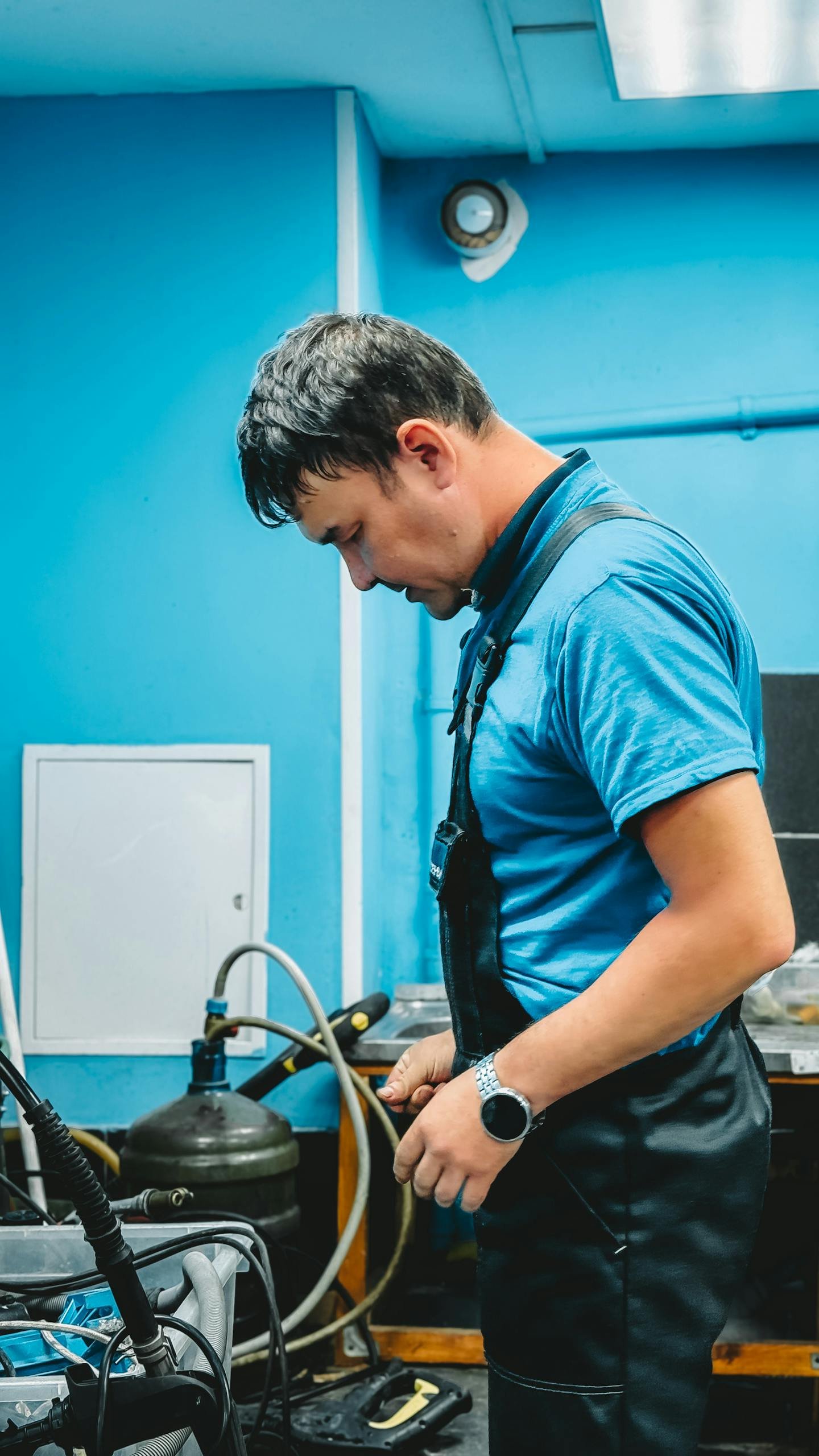 A male adult technician in a blue workshop setting, engaged in work.
