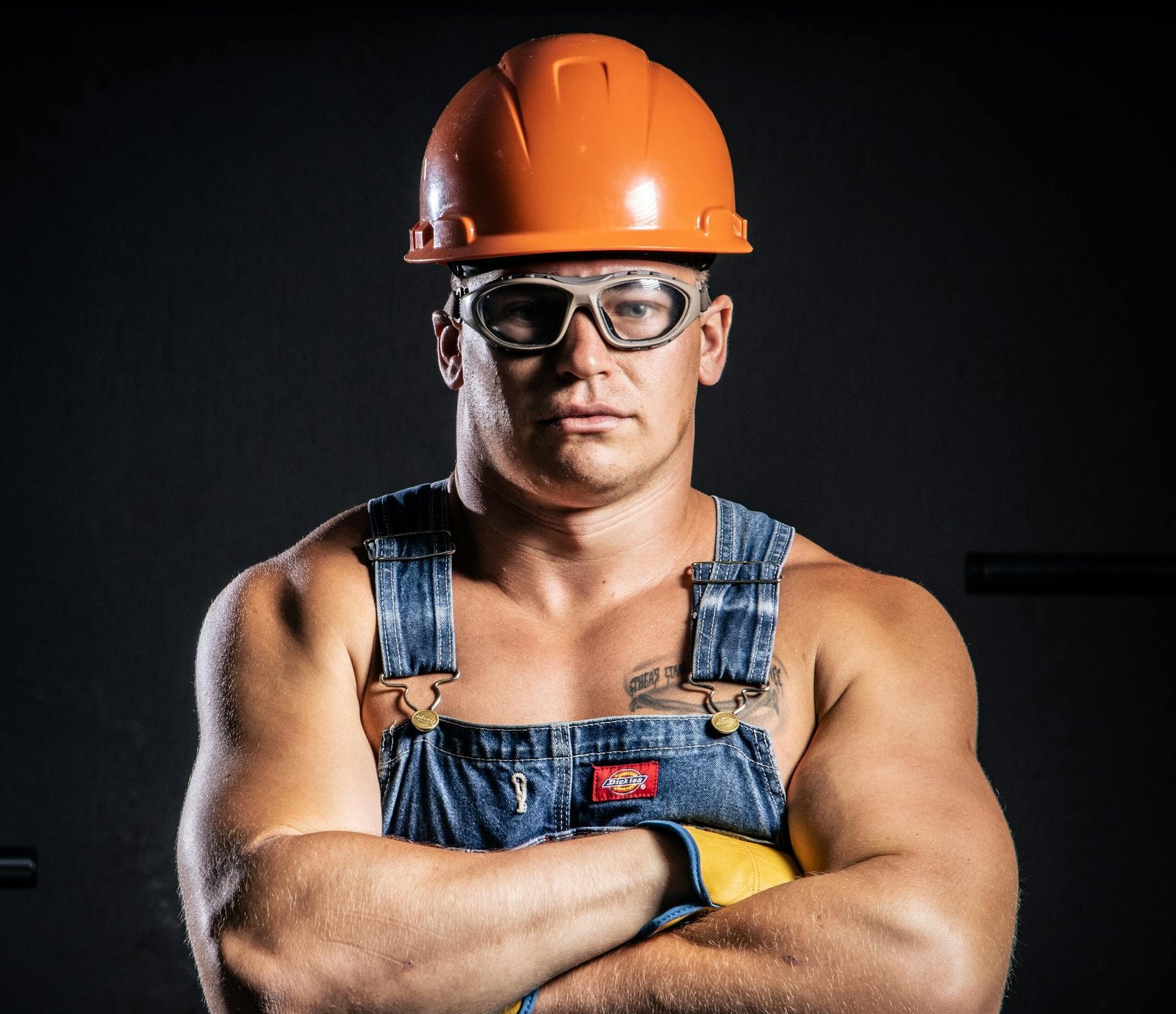Portrait of a muscular construction worker with arms crossed, wearing goggles and a hard hat.
